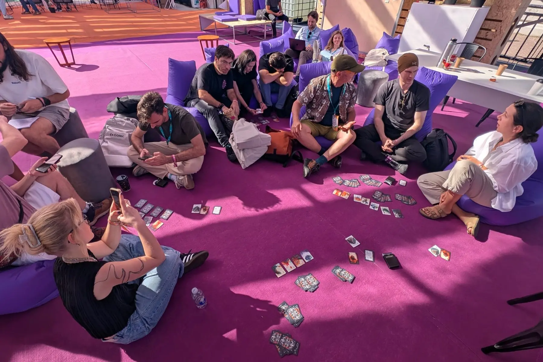 A circle of players on a purple floor at Devconnect, with cards from the deck spread between them.