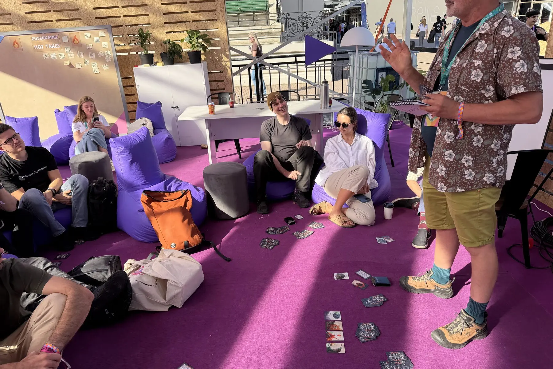 At the Governance Geeks hub, a player stands and talks over the cards on the floor while the group listens.