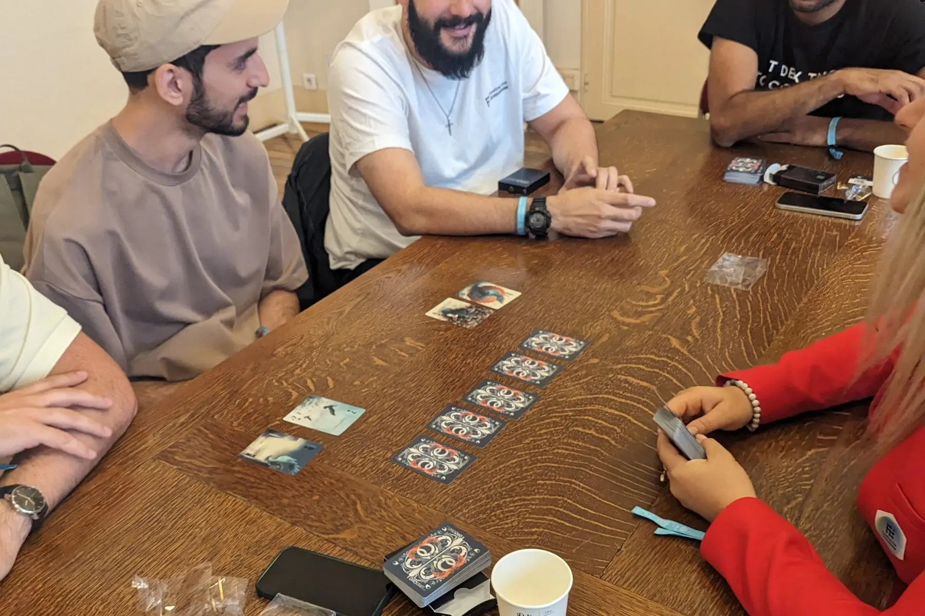 Players at a wooden table in Paris lay out a row of cards from the deck, backs up.